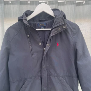 Jacka Ralph Lauren - Säljer nu denna vår jacka från Ralph Lauren i marinblå färg | Storlek Ungdom L vilket motsvarar XS i herr storlek | Skick utifrån bilderna jackan har några små defekter som syns på bilderna, annars inga andra | Huvan går att rulla in i jackan | Dma vid funderingar 💭