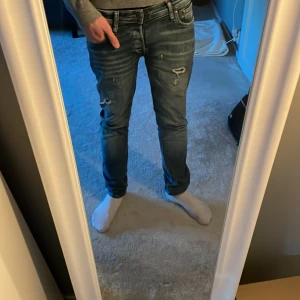 Blå slim fit jeans - Snygga blå slim fit jeans med slitna detaljer och en modern look. De har en klassisk femficksdesign och dragkedja. Perfekta för en stilren vardagsoutfit.