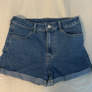 Blå jeansshorts med uppvikta ben - Snygga blå jeansshorts med klassisk femficksdesign och uppvikta ben. Perfekta för en avslappnad stil. De har en knapp och dragkedja framtill.