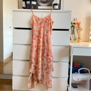 Super söt mönstad lång sommarklänning - Säljer en vacker långklänning från Xadrez i ett färgglatt mönster med inslag av rosa och beige. Klänningen är tillverkad i polyester, vilket ger den ett lätt och luftigt fall. Perfekt för sommarens varma dagar!