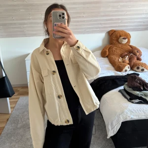Beige jacka med knappar - Säljer en stilren beige jacka med knappar framtill. Jackan har långa ärmar och en klassisk krage. Perfekt för vår och höst!