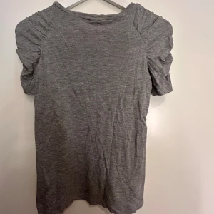 Grå topp med rynkade ärmar från h&m💗 - Säljer en stilren grå topp med rynkade korta ärmar. Perfekt för en avslappnad look. Toppen har en rund halsringning och är tillverkad i ett mjukt material. Skriv till mig om det är något💖köparen står ev.frakten