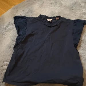 Mörkblå topp från C&A - Säljer en mörkblå topp från C&A. Den har korta ärmar med en liten volangdetalj. Perfekt för en avslappnad stil. Passar bra till jeans eller kjol.