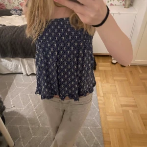 Blåmönstrad ärmlös topp - Säljer en söt blåmönstrad topp med justerbara axelband och smockdetaljer upptill. Toppen har en luftig passform och ett vågigt avslut nedtill. Perfekt för varma dagar!