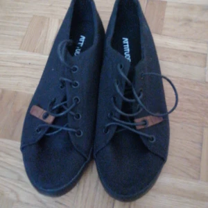 Svarta sneakers från Attitude - Snygga svarta sneakers från Attitude med snörning och bruna detaljer. Perfekta för en stilren look. Skorna har en klassisk design med rund tå och slitstark sula.