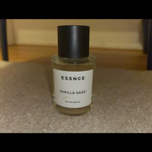 Essnce Vanilla Sass Eau de Parfum - Upptäck Essnce Vanilla Sass Eau de Parfum, en doft med en söt och kryddig vaniljton. Flaskan är elegant och rund med en svart kork och en stilren etikett. Perfekt för dig som älskar en varm och inbjudande doft. (Den är som ny bara två tre sprays har använts). 