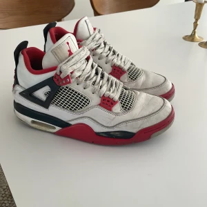 Nike Air Jordans i vitt och rött - Snygga Nike Air Jordans i vitt med röda och svarta detaljer. Skorna har snörning och en ikonisk design med synlig luftdämpning i sulan. Perfekta för dig som vill ha en klassisk sneaker med stil.