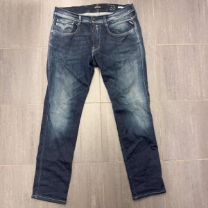 Blå jeans från Replay - Snygga blå jeans från Replay med en klassisk femficksdesign och lätt slitna detaljer. Perfekta för en avslappnad stil. Midjan är midwaist och passformen är normal. Priset kan diskuteras.
