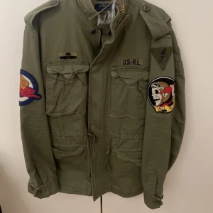 Grön jacka från Polo Ralph Lauren - Säljer en grön jacka från Polo Ralph Lauren. Jackan har dragkedja och knappar framtill samt snörning i midjan. Perfekt för en avslappnad stil.