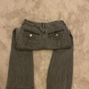Grå jeans med utsvängda ben från H&M - Snygga grå jeans från H&M med utsvängda ben och broderade detaljer på bakfickorna. De har en midwaist passform och är perfekta för en avslappnad stil. Jeansen har en klassisk femficksdesign och stängs med dragkedja och knapp.
