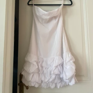 Vit axelbandslös klänning från Vila💘 - Säljer en elegant vit axelbandslös klänning från Vila. Klänningen har en volangdetalj vid fållen som ger en lekfull touch. Perfekt för sommarens festligheter!💘priset går att förhandla💘