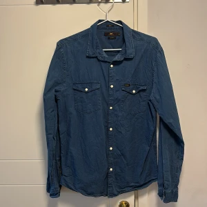 Blå jeansskjorta från Lee - Snygg blå jeansskjorta från Lee i slim fit. Skjortan har långa ärmar och knappar framtill samt på bröstfickorna. Perfekt för en stilren look.