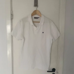 Vit pikétröja från Morris - Säljer en stilren vit pikétröja från Morris med korta ärmar och klassisk krage. Tröjan har en liten broderad detalj på bröstet och knappar framtill. Perfekt för en avslappnad men ändå uppklädd look. Passar M alldeles utmärkt. Skriv om ni har några övriga frågor🙌