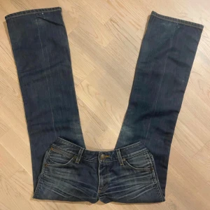 Blå jeans från Wrangler - Säljer ett par klassiska blå jeans från Wrangler. De har en snygg bootcut-stil och är tillverkade i slitstarkt denim. Baktill finns två fickor med det ikoniska W-broderiet. Perfekta för en avslappnad look.