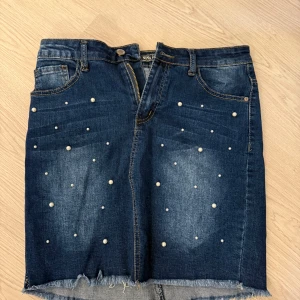 Jeanskjol med pärlor - Snygg jeanskjol från Nina med pärldetaljer och fransig nederkant. 