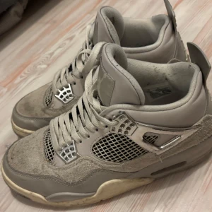 Jordan 4 - Säljer ett par grå Nike Air Jordans med snörning och ikonisk design. Skorna har en kombination av skinn och syntetmaterial med detaljer i silver. Perfekta för sneaker-entusiaster som vill ha en klassisk stil.