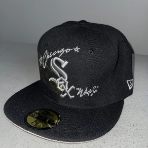 Chicago White Sox keps New Era 59FIFTY - Snygg svart keps från New Era 59FIFTY med broderad Chicago White Sox-logga och text i vitt. Platt skärm med ljus undersida och broderad World Series-patch på sidan. Klassisk streetstyle med coola detaljer, perfekt för dig som gillar sport och stil.