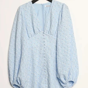 Ljusblå blommig klänning från Adoore - Supersöt ljusblå klänning från Adoore med små vita blommor, v-ringning och knappar framtill. Den korta modellen!🩷