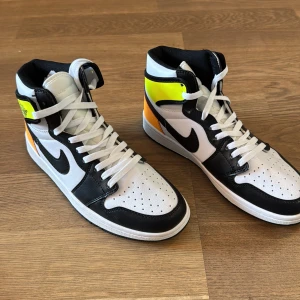Nike Air Jordan 1 High svart/vit/gul - Nike Air Jordan 1 High sneakers i svart, vitt, gult och orange. Klassisk high-top siluett med svart swoosh, perforerad tå och vita skosnören. Ovandel i skinn och syntet, svart yttersula och färgstarka detaljer på hälen. Perfekta för dig som vill sticka ut.