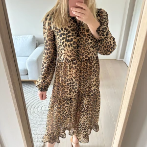 Nakd strl 38 Leopardmönstrad långklänning strandklänning - Strandklänning / långklänning med leopardmönster. Klänningen har långa ärmar, knappar framtill och volangkant nertill. Materialet är tunt och luftigt, perfekt för varma dagar. Snygg till sandaler och hatt för en cool sommarlook. Ganska genomskinlig så bäst som strandklänning. Strl 38 (passar 36/38)