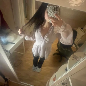 Ljuslila prickig blus med volang - Supersöt ljuslila blus med prickigt mönster, v-ringning och volangdetaljer längs halsringningen och midjan. Blusen har långa, transparenta ärmar och dragkedja i sidan för enkel påklädning. Perfekt för dig som gillar romantisk och feminin stil.