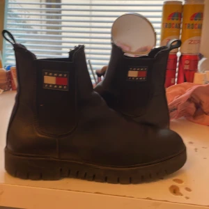 Svarta chelsea boots från Tommy Jeans - Chunky svarta chelsea boots från Tommy Jeans med grov sula och klassisk logga på sidan. Skorna är i skinn och har elastiska paneler på sidorna för enkel påtagning. Perfekta för dig som vill ha en stilren men edgy look. Jätte sköna och inuti 