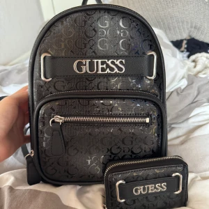Svart ryggsäck och plånbok från Guess - jag har inte använt den mer än 24 timmar. det finns kvitto om man vill se. Snygg svart ryggsäck från Guess med matchande plånbok. Väskan har silverfärgade detaljer, dragkedja framtill och tydligt Guess-logga i metall. 