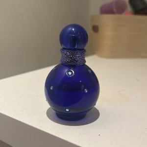Britney Spears Midnight Fantasy 30ml - Säljer en ikonisk parfym, Midnight Fantasy av Britney Spears. Flaskan är rund och djupblå med glittrande stenar och ett dekorativt halsband runt halsen. Rymmer 30 ml och är perfekt för dig som gillar söta och mystiska dofter.