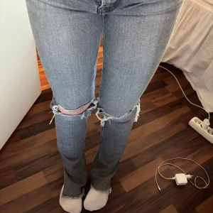 Grå ripped jeans från Zara, strl 34 - Säljer ett par gråa jeans från Zara i storlek 34. De är högmidjade med raka ben och har slitna detaljer och hål vid knäna.