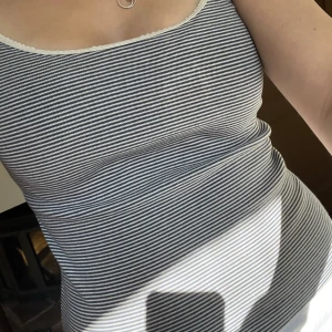 Randig linnetopp med spetskant - Supersöt randig linnetopp i blått och vitt med tunna axelband och en fin spetskant upptill. Perfekt för varma dagar eller att styla lager på lager. Toppens material känns mjukt och följsamt mot huden.