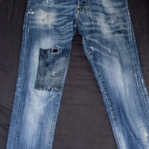 Dsquared2 jeans  - Snygga Dsquared2 Skinny Dan jeans i blå tvätt med slitningar, lagningar och patchdetaljer. Klassisk femficksmodell med skinny fit och låg midja. Jeansen har coola slitna partier och tydliga kontrastsömmar. Perfekta för dig som gillar streetstyle och edgy look.