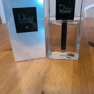 Dior Homme Eau de Toilette 150ml - Dior Homme Eau de Toilette i stor flaska på 150 ml. Parfymen kommer i en elegant, transparent glasflaska med svart och silverdetaljer samt tillhörande silverfärgad kartong. Doften är maskulin och modern, perfekt för dig som gillar exklusiva märkesparfymer.