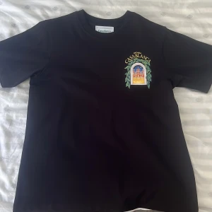 Svart Casablanca t-shirt med tryck - Svart t-shirt från Casablanca med färgglatt tryck av ett fönster och byggnad både fram och bak. Klassisk passform, rund hals och korta ärmar. Tillverkad i 100% ekologisk bomull. Perfekt för dig som vill sticka ut med en unik design. Den är helt Äkta och har köpt den från Casablanca Hemsida.