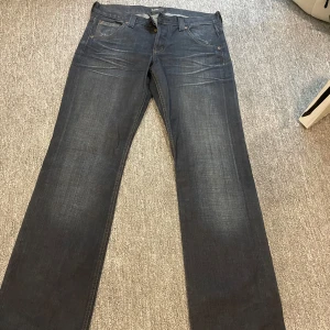 Mörkblå jeans från Lee - Säljer ett par klassiska mörkblå jeans från Lee med raka ben och snygga slitningar framtill. Jeansen har fem fickor, gylf med dragkedja och Lee-logga på bakfickan samt läderpatch i midjan. Perfekta för en stilren och avslappnad look.
