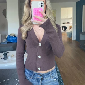 Kofta  - Säljer en brun kofta från Noisy May med knappar  och v-ringad hals. Koftan är stickad i mjukt material och har långa ärmar. Perfekt att styla med jeans.