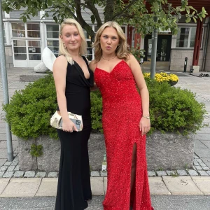 Röd glittrig balklänning med snörning - Säljer en lång röd glittrig balklänning med smala axelband, v-ringning och snygg slits framtill. Klänningen har snörning i ryggen för perfekt passform och är täckt av paljetter som ger ett riktigt statement. Perfekt för bal eller fest!