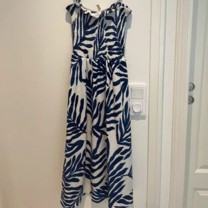 Blåvit långklänning från H&M - Supersnygg långklänning från H&M med blått och vitt  mönster. Klänningen har smala axelband, smockad överdel och ett flowy fall. Perfekt för sommarens varma dagar och ger en fräsch vibe med sitt coola mönster. Använd fåtal gånger 