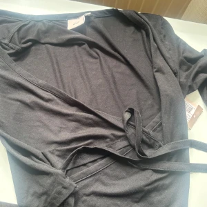 Svart omlotttröja från Nelly - Svart omlott tröja från Nelly i mjuk bomull. Tröjan har lång ärm, v-ringning och knyt i midjan för en snygg passform. Enkel och stilren design som passar perfekt till många olika looks. Jag säljer den för jag inte riktigt tyckte om den, den är aldrig använd och prislappen sitter kvar!💕