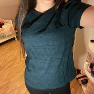 Mörkgrön blus med puffärm - Säljer en mörkgrön blus med korta puffärmar och diskret struktur i tyget. Blusen har rund halsringning och en loose passform som ger en avslappnad vibe. Perfekt att styla med jeans eller kjol för en cool look.