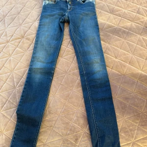 Blå skinny jeans från Replay - Säljer ett par blå skinny jeans från Replay med klassisk femficksdesign och snygga slitningar. Jeansen har normal passform i midjan och är tillverkade i stretchig denim för extra komfort. Perfekta för dig som gillar en tajt look och vill ha ett par stilrena jeans.
