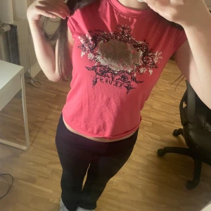 Rosa croppad topp från Feluna - Säljer en rosa croppad topp med korta ärmar och ett stort tryck i silver och svart framtill. Toppen har en rund halsringning och är gjord i mjuk bomull, perfekt för en cool och avslappnad stil.