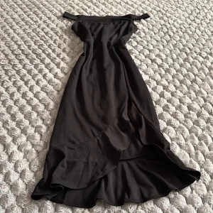 Svart offshoulder långklänning Shein - Supersnygg svart långklänning från Shein med offshoulder-design och volangdetalj nertill. Klänningen har en figurnära passform och dragkedja i ryggen. Perfekt för dig som vill sticka ut med en elegant och stilren look.