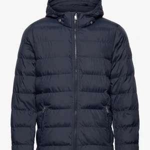 Mörkblå pufferjacka från Matinique - Snygg mörkblå pufferjacka från Matinique med huva och dragkedja framtill. Jackan har quiltad design, två fickor med dragkedja och en glansig olivgrön insida. Perfekt för kalla dagar och riktigt skön att bära.