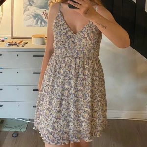 Blommig kort sommarklänning från NA-KD - Supersöt kort klänning med blommigt mönster.. Klänningen har omlott v-ringning, smala axelband och lätt rynkad kjol. Perfekt för varma dagar. Använd fåtal gånger. 