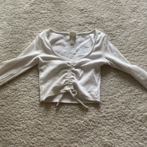 Vit croppad topp med snörning H&M XS - Säljer en jättesöt vit croppad topp från H&M i ribbad bomull☺️ Toppen har lång ärm, v-ringning och snygg snörning framtill som ger en cool rynkad effekt. Perfekt att styla med höga jeans eller kjol för en trendig look💕 skriv alltid till mig vid frågor. Ni betalar frakt☺️