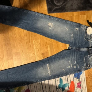 Replay Anbass blå slitna jeans äkta - Säljer ett par blå Replay Anbass jeans med snygga slitningar och tvättad look. Jeansen har klassisk femficksmodell, normal passform och är tillverkade i mjukt jeansmaterial. Perfekta för dig som gillar en avslappnad och trendig stil.