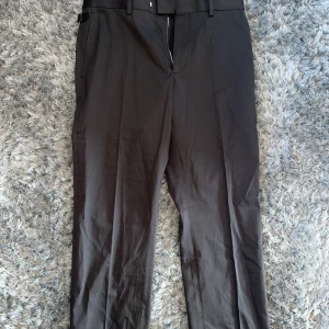 Svarta kostymbyxor från Louis Vuitton - Snygga svarta kostymbyxor från Louis Vuitton, tillverkade i Italien. Byxorna har raka ben, diskret bälte med metallspänne och klassisk passform. Materialet är mjukt och exklusivt, perfekt för dig som vill ha en stilren look.