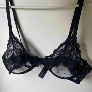 Svart spetsig bralette från Nelly - Supersnygg svart bralette från Nelly med transparent spets och blommigt mönster. Toppens tunna axelband och detaljerade spets ger en riktigt trendig vibe. Perfekt för att styla lager på lager eller som statement-piece till din outfit.