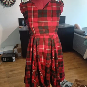 Röd och svart rutig kortklänning - Supersnygg röd och svart rutig klänning med markerad midja och utställd kjol. Klänningen är ärmlös och har dragkedja i ryggen. Perfekt för dig som gillar retrovibbar och vill sticka ut med ett klassiskt rutmönster.