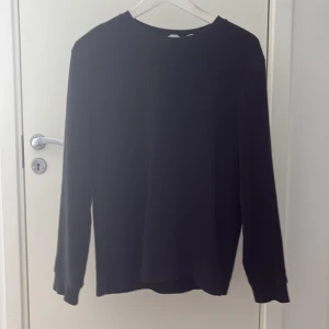 Svart långärmad tröja Dobber, i bomull S - En basic svart långärmad tröja i storlek S men passsr även XS. Tröjan har rund halsringning och är tillverkad i mjuk bomull. Perfekt att styla med jeans eller under en jacka. Enkel och stilren design som funkar till det mesta. Skick 9/10